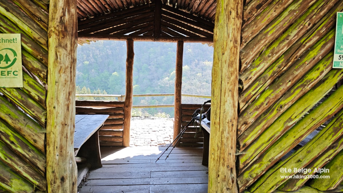 Interieur d'un abri de randonneurs en rondins de bois, ouvert sur la vallee, batons de marche