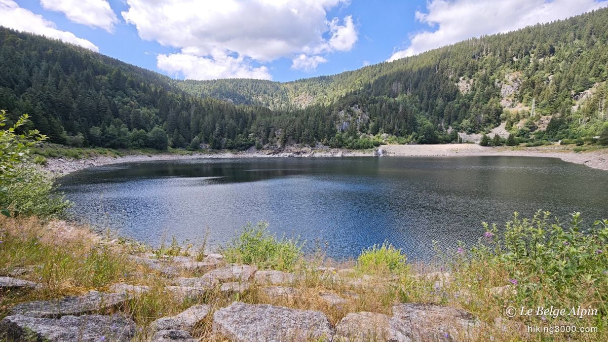 A first lake held back by its dam, in the hollow of the wooded slopes